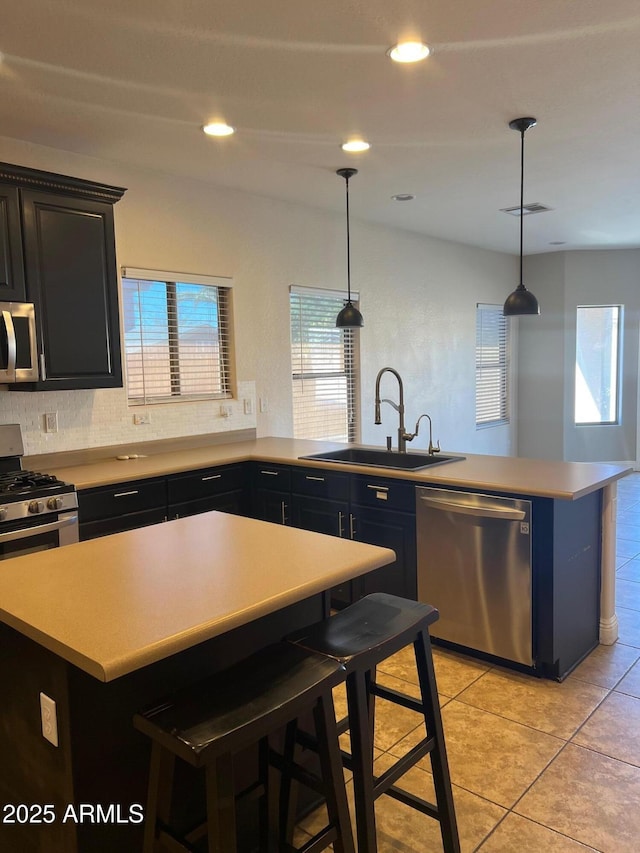 kitchen with sink, hanging light fixtures, a kitchen breakfast bar, a kitchen island, and stainless steel appliances