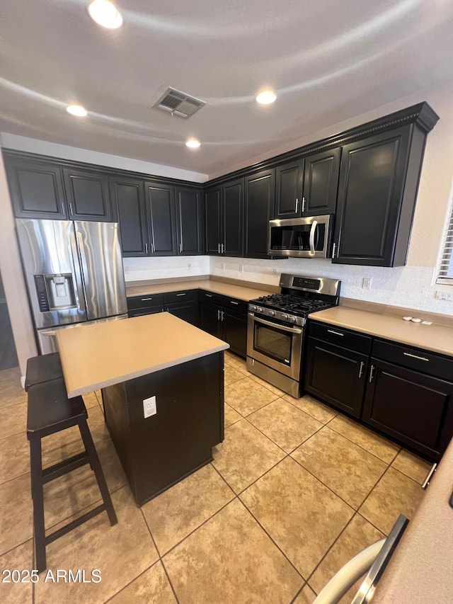 kitchen with light tile patterned flooring, a kitchen bar, tasteful backsplash, a center island, and stainless steel appliances