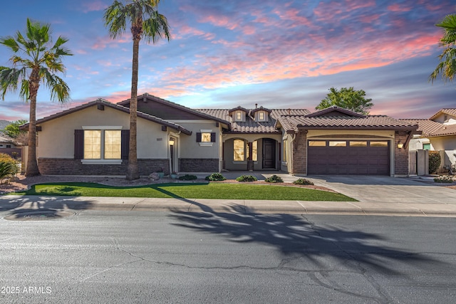 mediterranean / spanish-style home with a garage, a tile roof, driveway, stone siding, and stucco siding