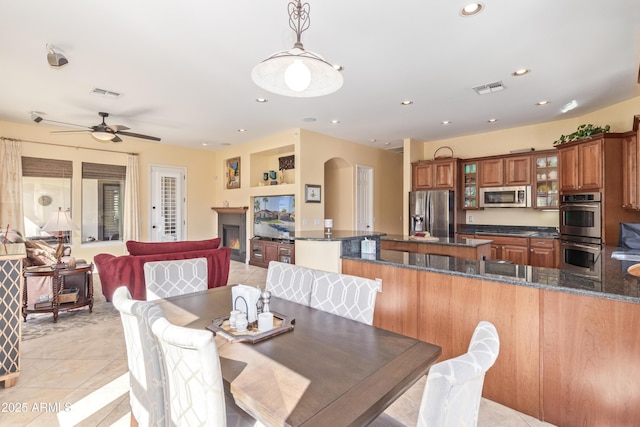 dining room featuring arched walkways, light tile patterned floors, recessed lighting, visible vents, and a lit fireplace