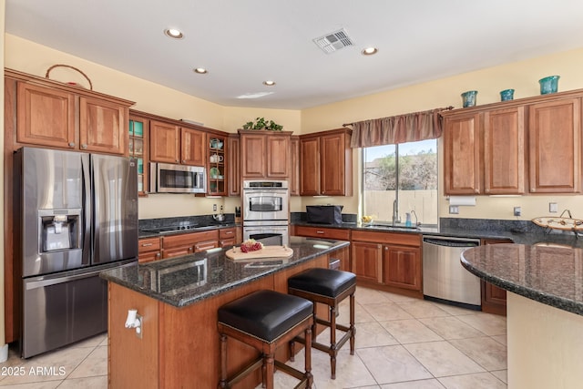 kitchen featuring a sink, a center island, appliances with stainless steel finishes, brown cabinets, and glass insert cabinets