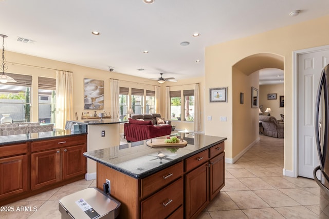 kitchen with light tile patterned floors, arched walkways, dark stone countertops, and a center island