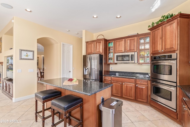 kitchen with appliances with stainless steel finishes, brown cabinetry, glass insert cabinets, and a center island