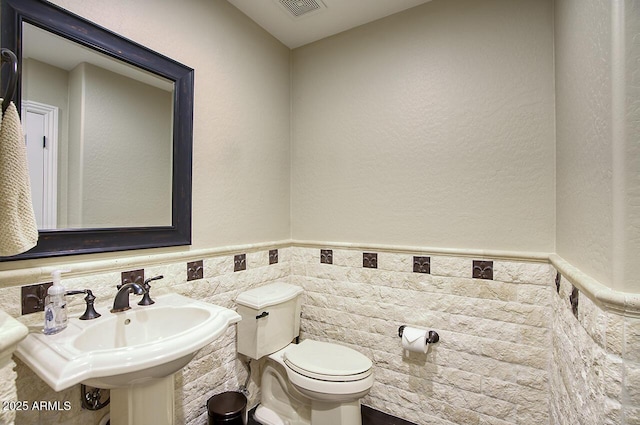 bathroom featuring visible vents, tile walls, a sink, a wainscoted wall, and toilet