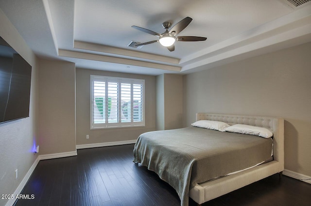 bedroom with visible vents, baseboards, ceiling fan, dark wood-style floors, and a tray ceiling