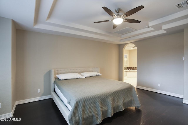 bedroom with visible vents, arched walkways, wood finished floors, a raised ceiling, and baseboards
