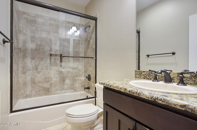 bathroom with toilet, a textured wall, combined bath / shower with glass door, and vanity