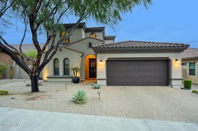 mediterranean / spanish house with decorative driveway, a garage, stucco siding, and a tiled roof