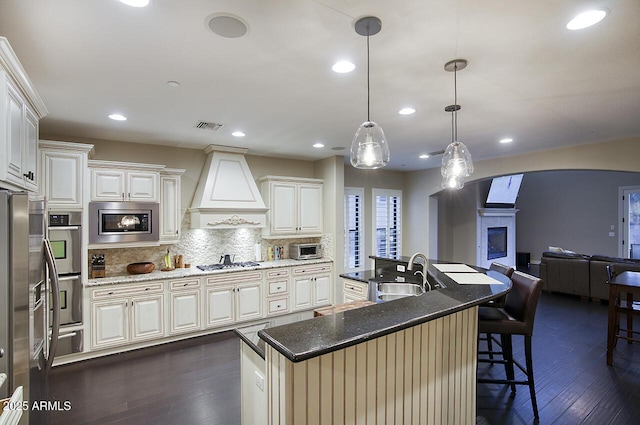 kitchen featuring visible vents, dark wood-style floors, premium range hood, a sink, and stainless steel appliances