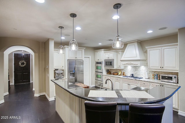 kitchen featuring decorative backsplash, custom exhaust hood, baseboards, arched walkways, and appliances with stainless steel finishes