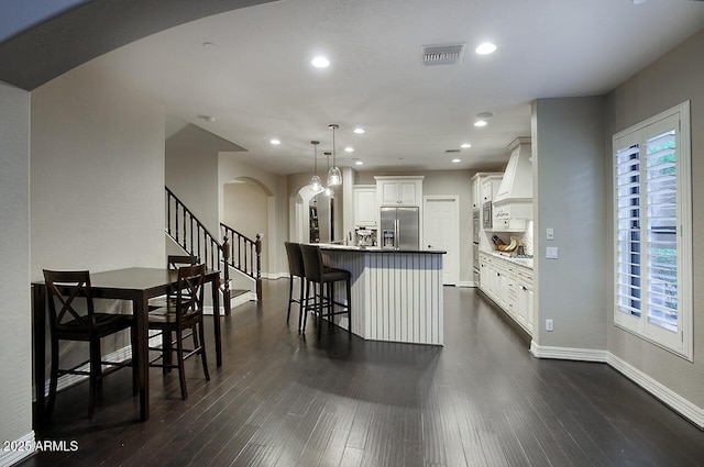 kitchen featuring visible vents, custom exhaust hood, a breakfast bar area, stainless steel fridge with ice dispenser, and arched walkways