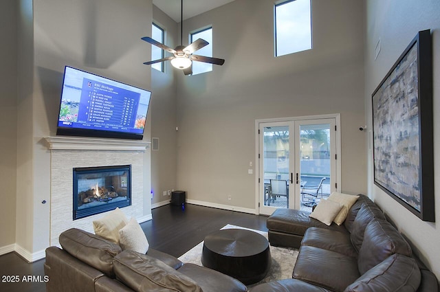 living room featuring dark wood-style flooring, a stone fireplace, a high ceiling, french doors, and a ceiling fan