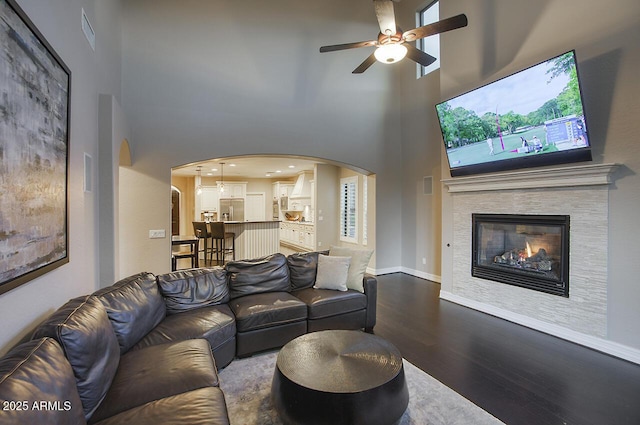 living area with ceiling fan, dark wood finished floors, a glass covered fireplace, a towering ceiling, and visible vents