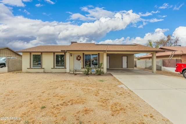 ranch-style home with driveway, roof mounted solar panels, fence, and an attached carport