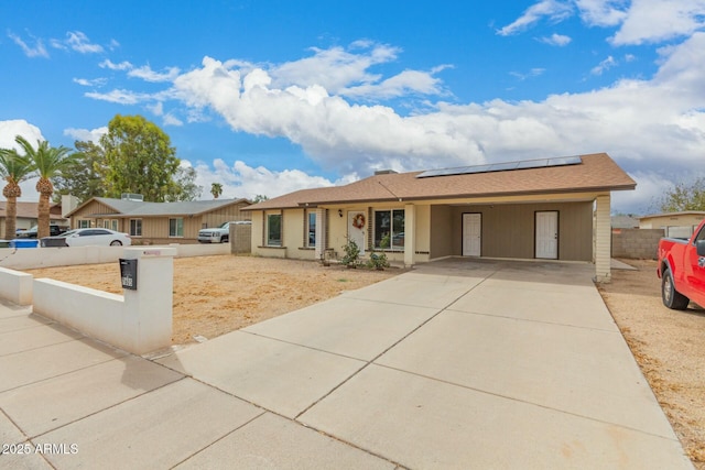 single story home with fence, an attached carport, solar panels, and concrete driveway