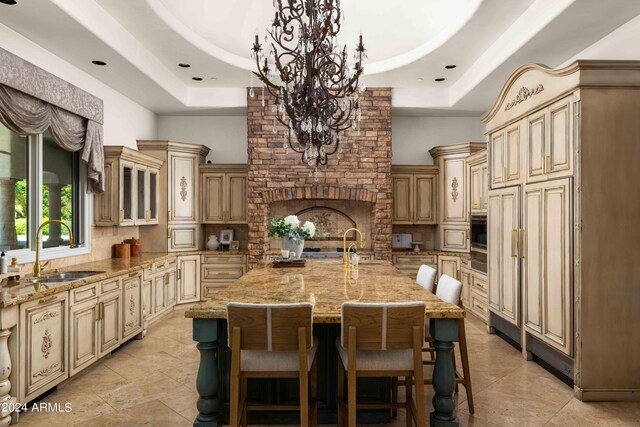 kitchen with a kitchen island with sink, light stone counters, a tray ceiling, and sink