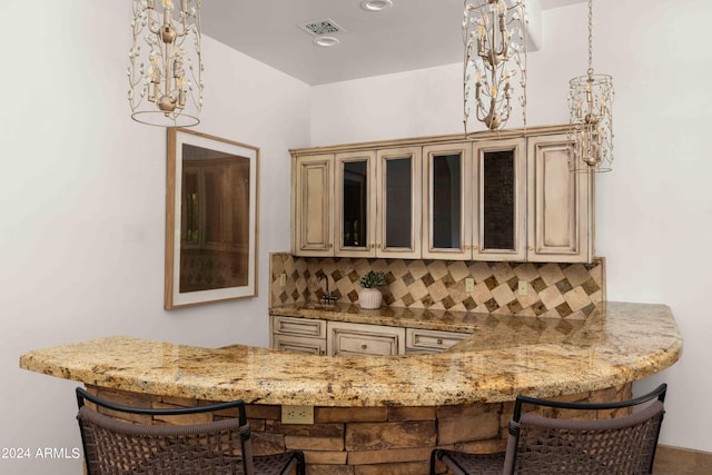 bar with light stone counters, backsplash, and cream cabinetry