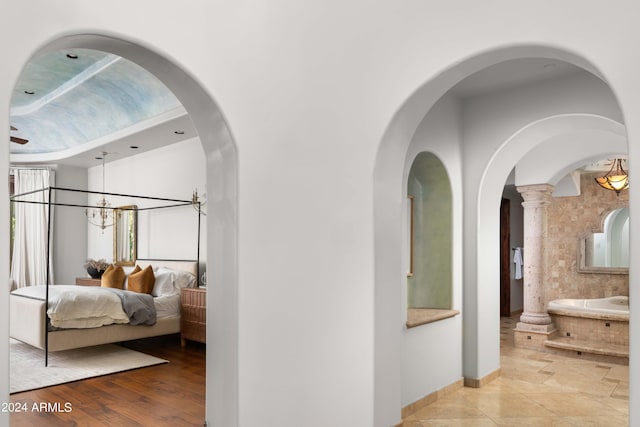 hallway featuring light wood-type flooring, ornate columns, and a notable chandelier