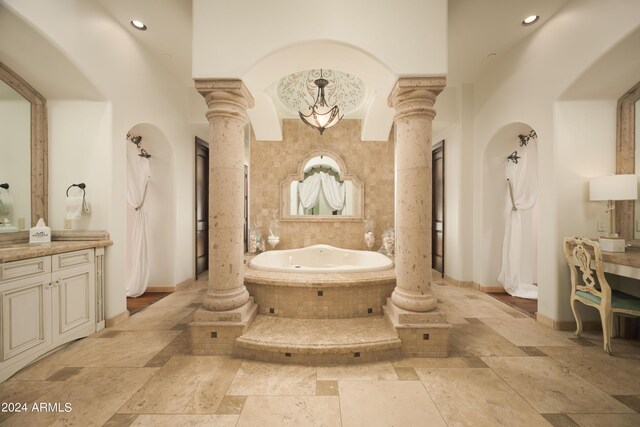 bathroom featuring vanity, a relaxing tiled tub, and ornate columns