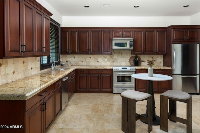 kitchen with a breakfast bar area, appliances with stainless steel finishes, tasteful backsplash, sink, and light stone counters