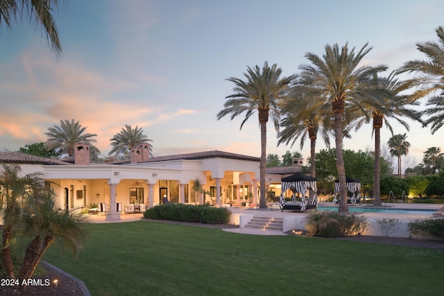 back house at dusk with a patio area and a lawn