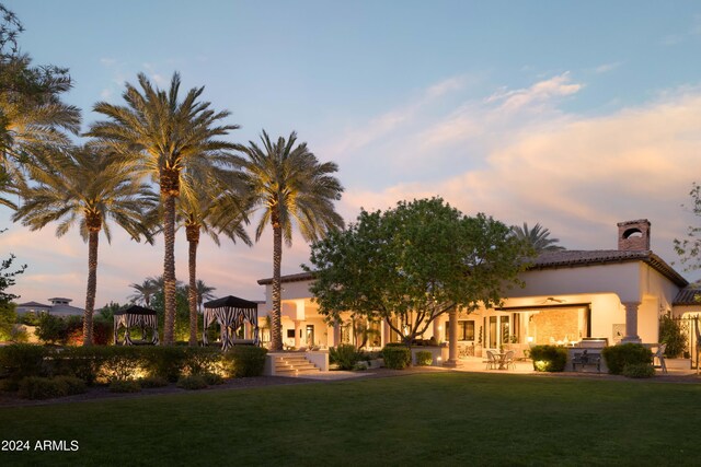 back house at dusk featuring a yard and a patio