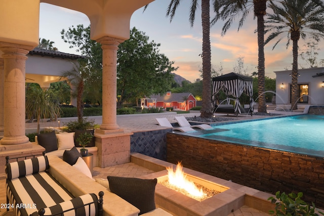 pool at dusk featuring a fire pit, a patio area, pool water feature, and a gazebo