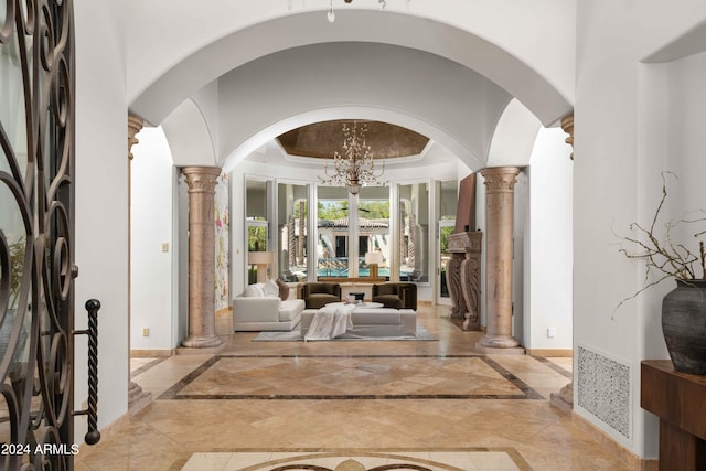 foyer entrance with a tray ceiling, an inviting chandelier, and decorative columns