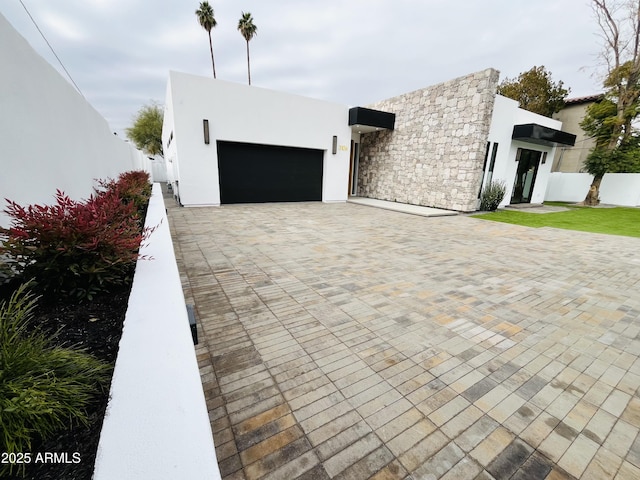 view of front of home featuring decorative driveway, an attached garage, fence, and stucco siding