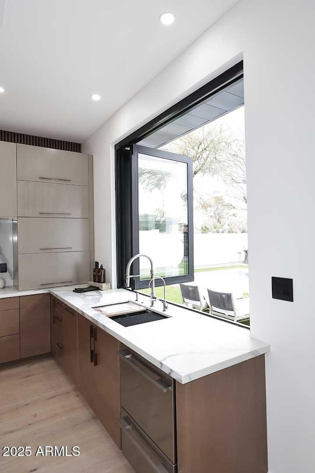 kitchen with light stone counters, recessed lighting, a sink, light wood-style floors, and dishwasher