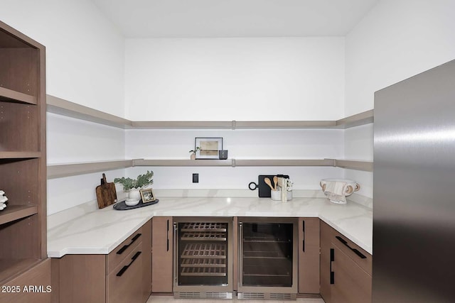 kitchen with beverage cooler, open shelves, light stone counters, and stainless steel fridge