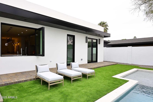 back of house featuring an outdoor pool, a lawn, fence, and stucco siding