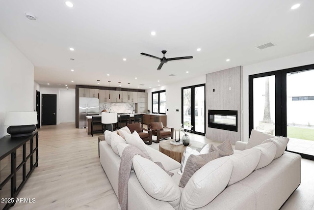 living room with a large fireplace, visible vents, a ceiling fan, light wood-type flooring, and recessed lighting