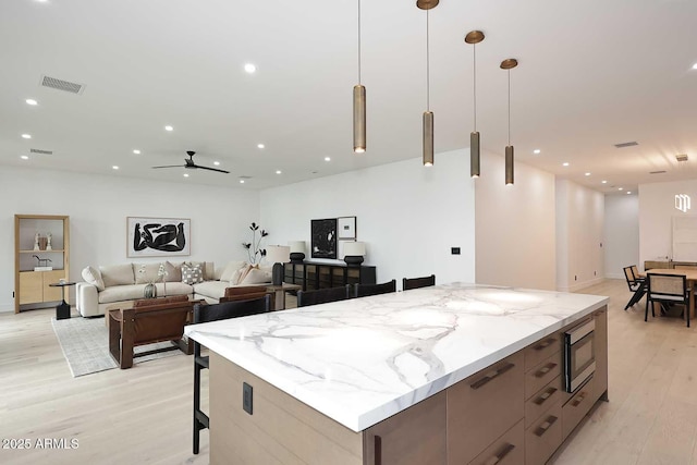 kitchen featuring a large island, modern cabinets, stainless steel microwave, open floor plan, and hanging light fixtures