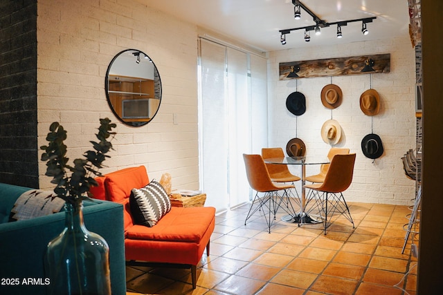 dining area with tile patterned flooring, rail lighting, and brick wall