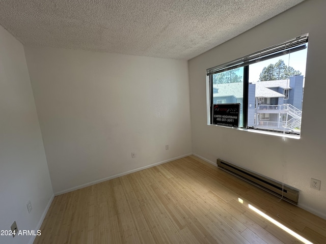 unfurnished room featuring a textured ceiling, light hardwood / wood-style floors, and baseboard heating