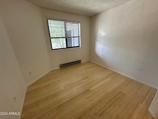 empty room with light wood-type flooring, a textured ceiling, and a baseboard heating unit