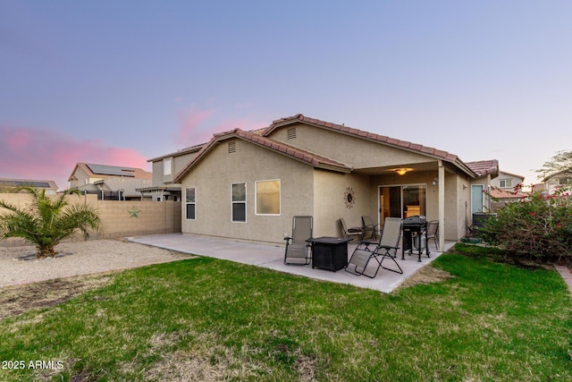 back of house at dusk featuring a yard, a patio area, a fenced backyard, and stucco siding