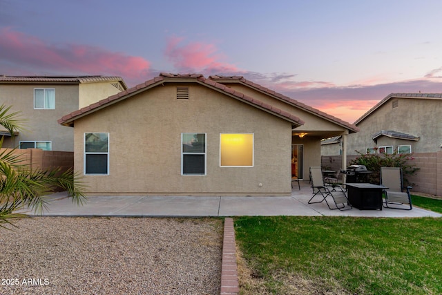 back of property at dusk featuring a tile roof, fence, a yard, a patio area, and stucco siding