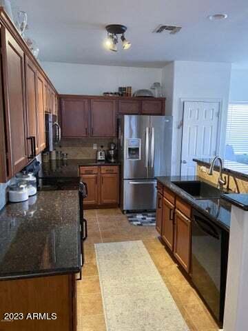 kitchen featuring stainless steel appliances, light tile patterned floors, dark stone counters, sink, and tasteful backsplash