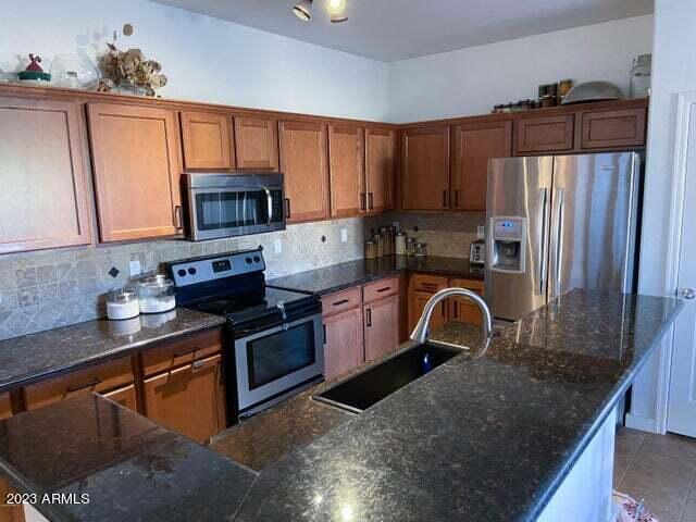 kitchen with stainless steel appliances, backsplash, sink, and a kitchen island with sink