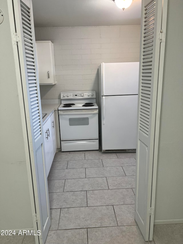 kitchen featuring white appliances, light tile patterned flooring, and white cabinets