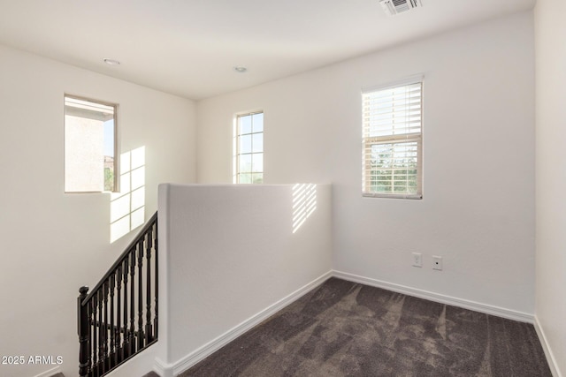 spare room with dark carpet, plenty of natural light, visible vents, and baseboards