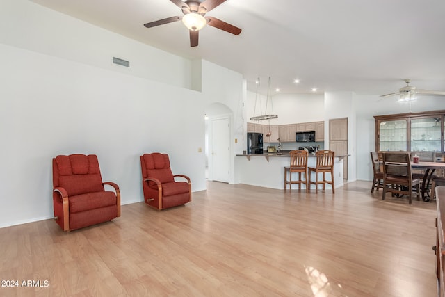 living area with light hardwood / wood-style floors, ceiling fan, and high vaulted ceiling