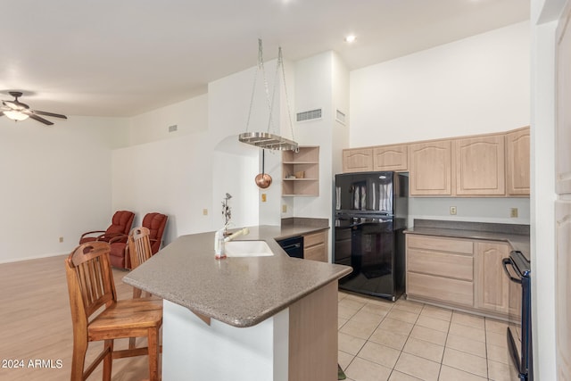 kitchen with kitchen peninsula, light hardwood / wood-style flooring, black appliances, a kitchen breakfast bar, and a high ceiling