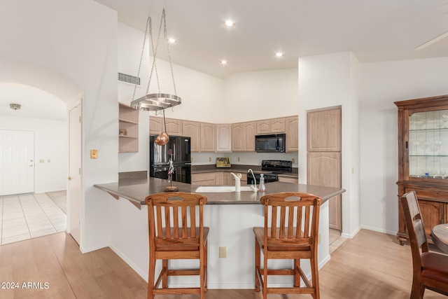 kitchen featuring a kitchen breakfast bar, black appliances, kitchen peninsula, and light hardwood / wood-style flooring