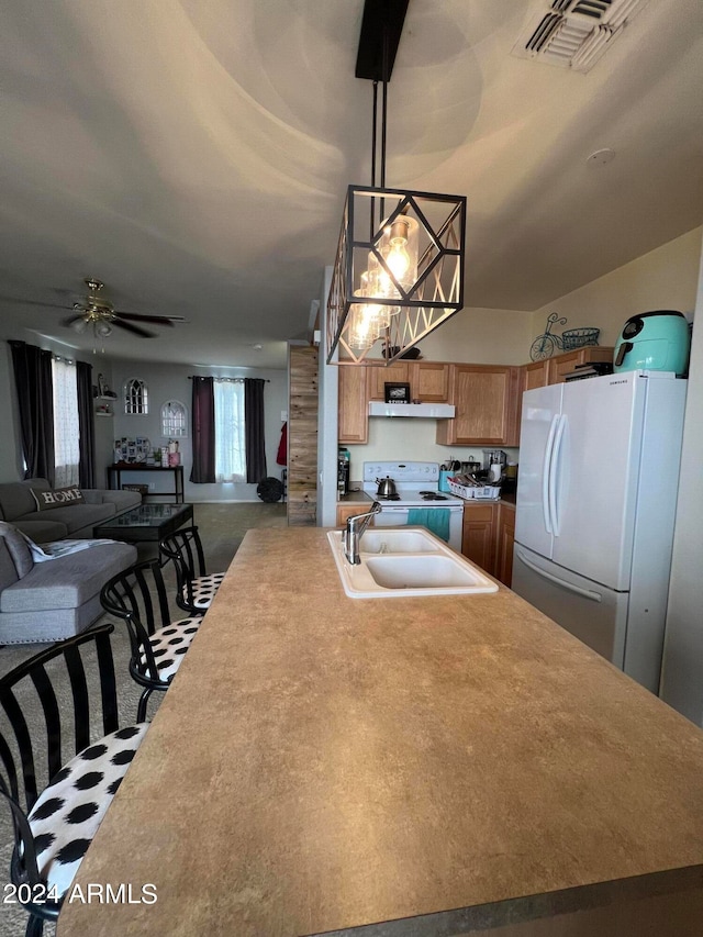 kitchen with sink, ceiling fan with notable chandelier, hanging light fixtures, carpet floors, and white appliances