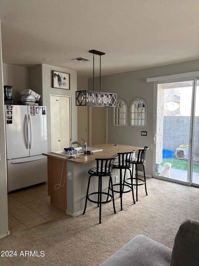 kitchen with an island with sink, carpet floors, stainless steel refrigerator, pendant lighting, and sink