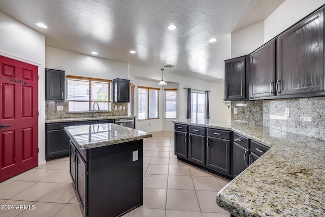 kitchen with a center island, hanging light fixtures, stainless steel dishwasher, sink, and light stone counters