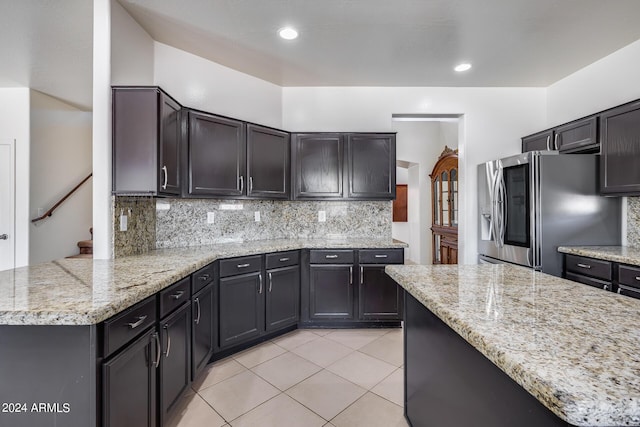 kitchen with kitchen peninsula, tasteful backsplash, light stone counters, light tile patterned flooring, and stainless steel refrigerator